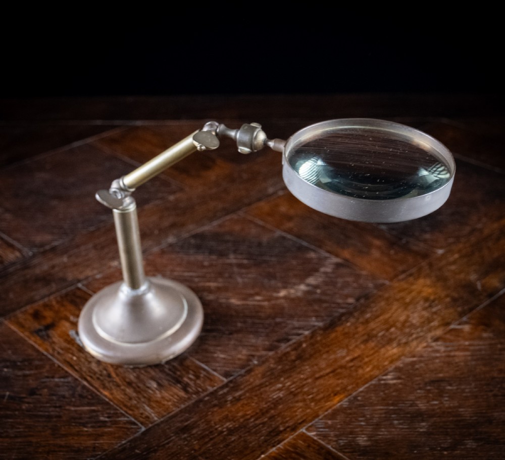 An antique Edwardian brass magnifying glass featuring an adjustable articulated arm and a circular weighted base. View IV