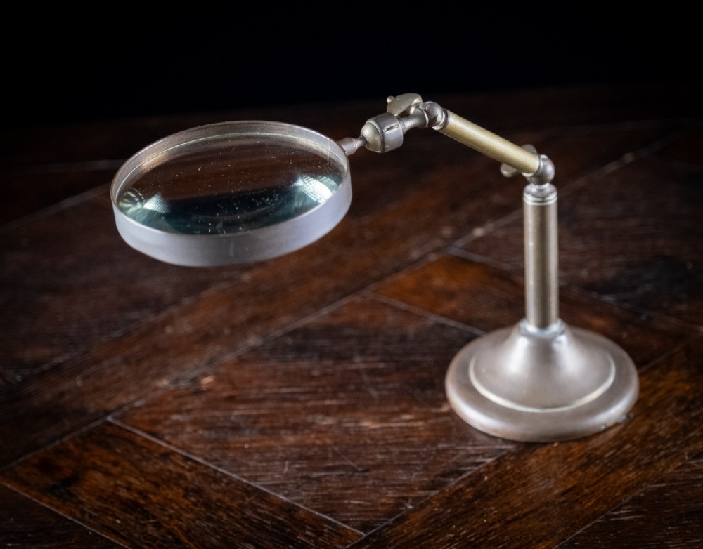 An antique Edwardian brass magnifying glass featuring an adjustable articulated arm and a circular weighted base. View V
