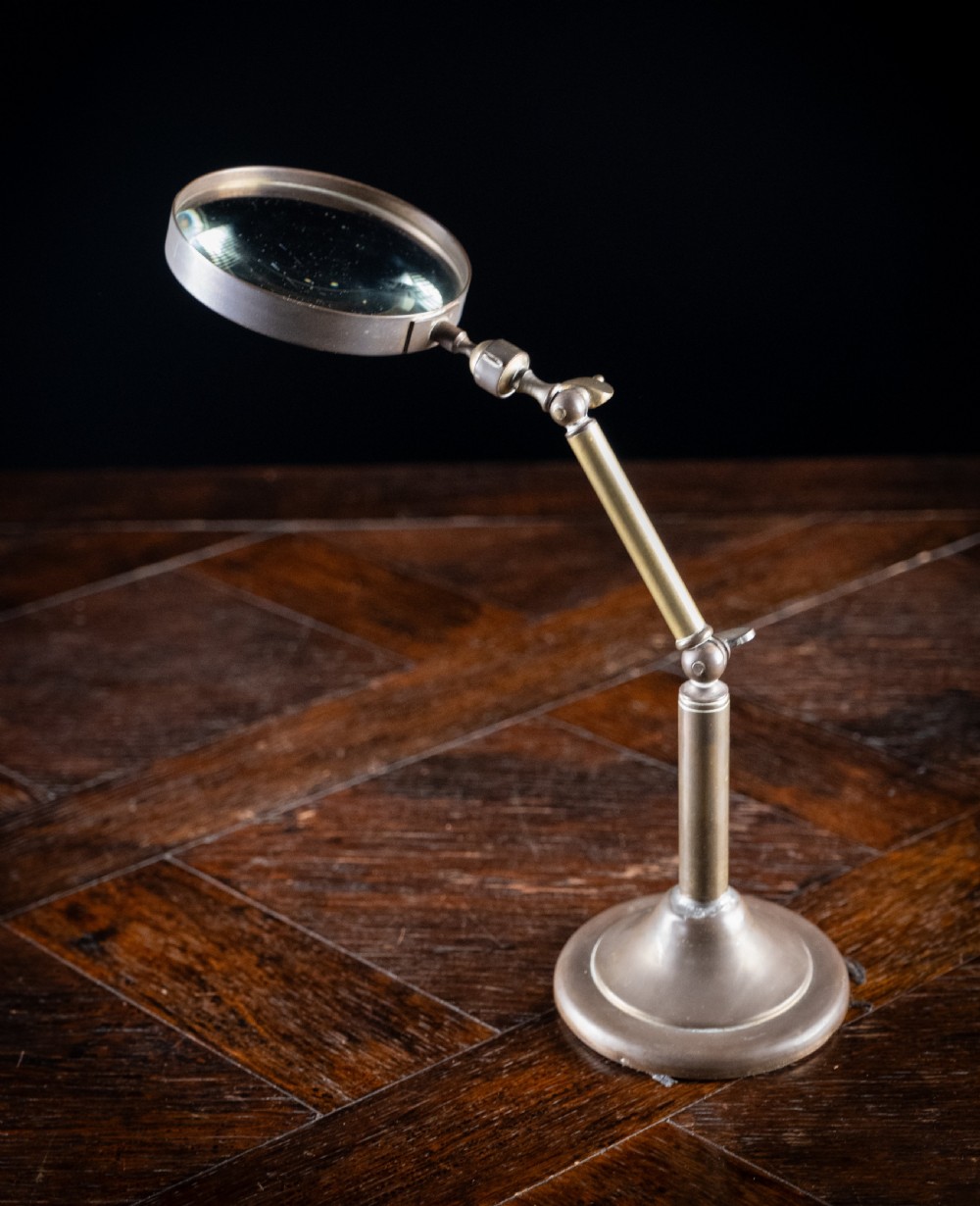 An antique Edwardian brass magnifying glass featuring an adjustable articulated arm and a circular weighted base. View VI