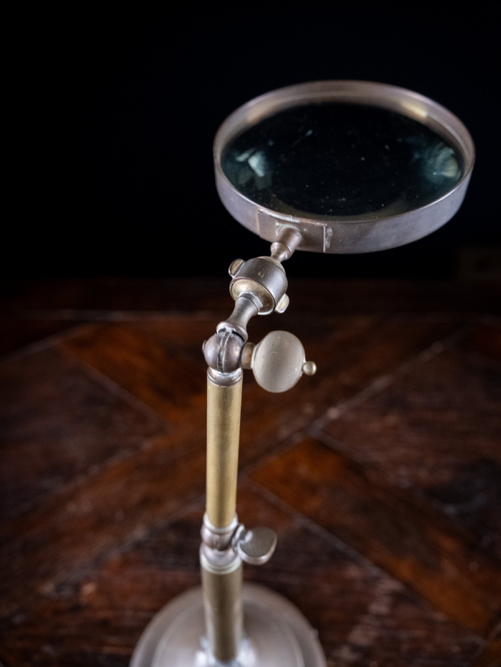 An antique Edwardian brass magnifying glass featuring an adjustable articulated arm and a circular weighted base. View VII