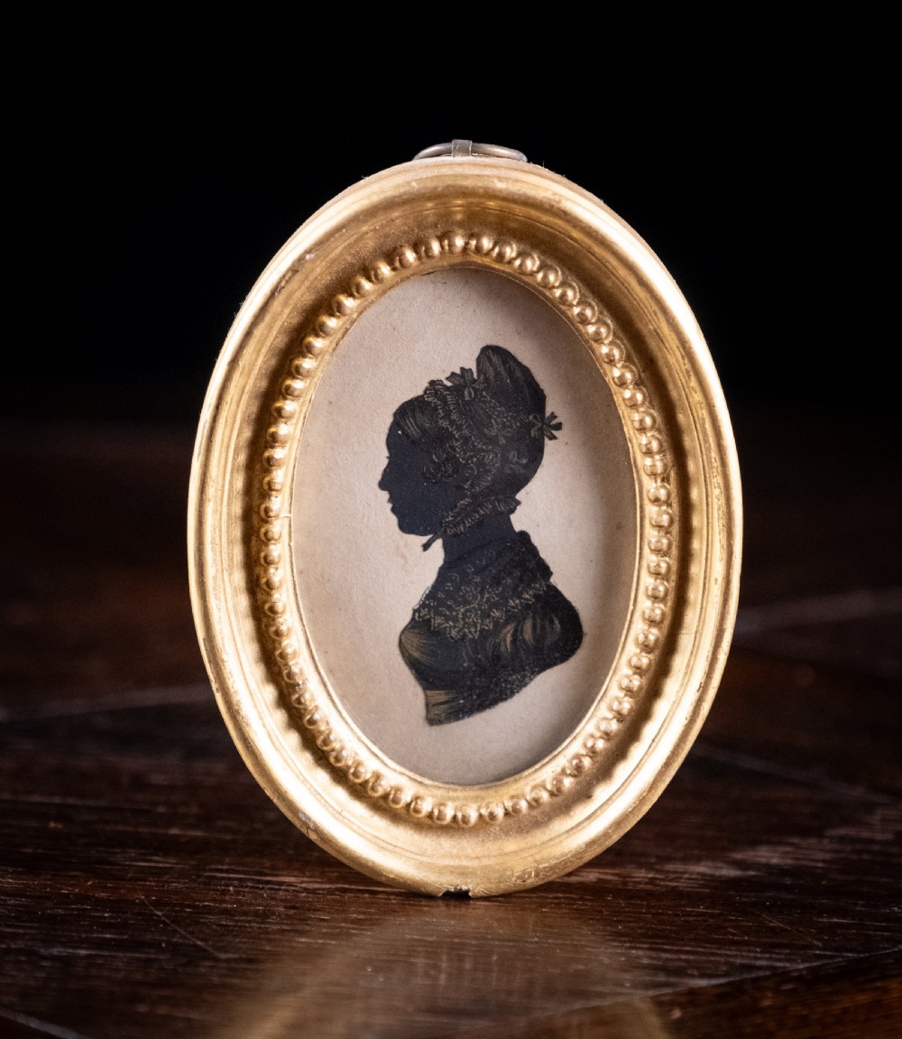 An oval early nineteenth-century silhouette portrait of a lady shown in profile with gold detailing, housed in a beaded gilded frame.