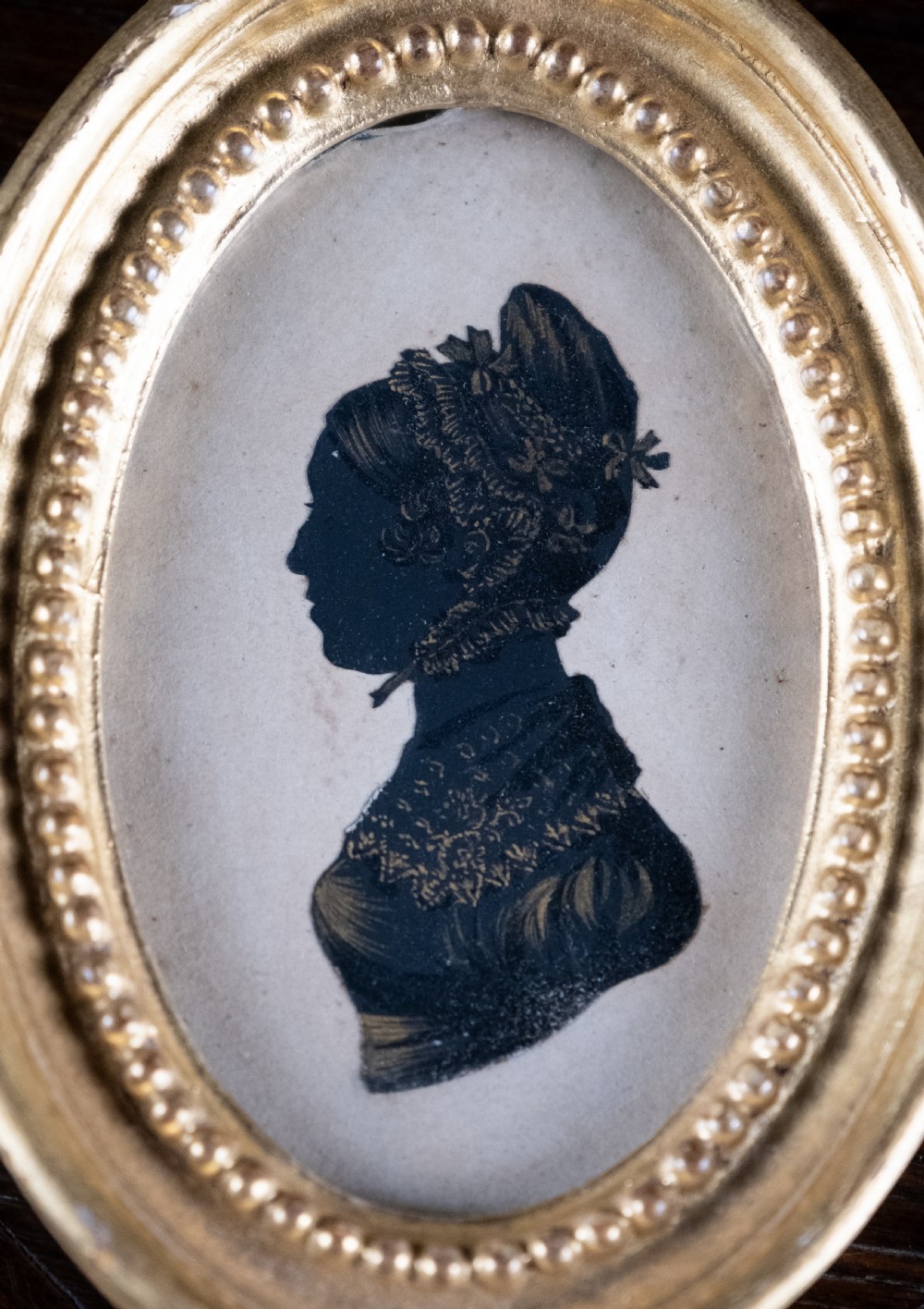 An oval early nineteenth-century silhouette portrait of a lady shown in profile with gold detailing, housed in a beaded gilded frame. View II