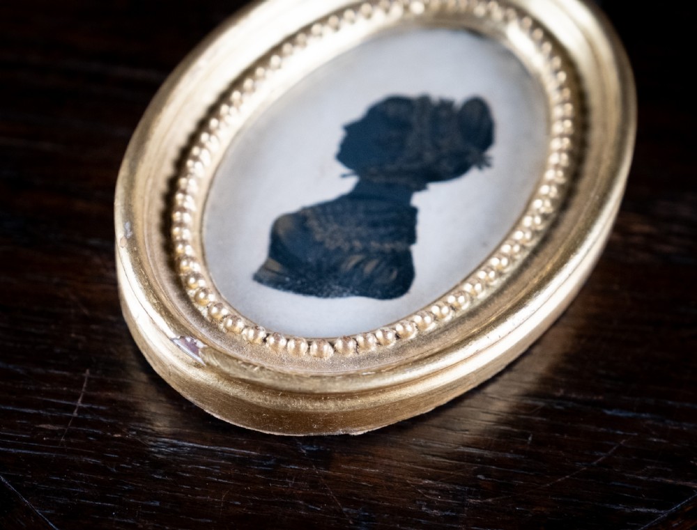 An oval early nineteenth-century silhouette portrait of a lady shown in profile with gold detailing, housed in a beaded gilded frame. View IV