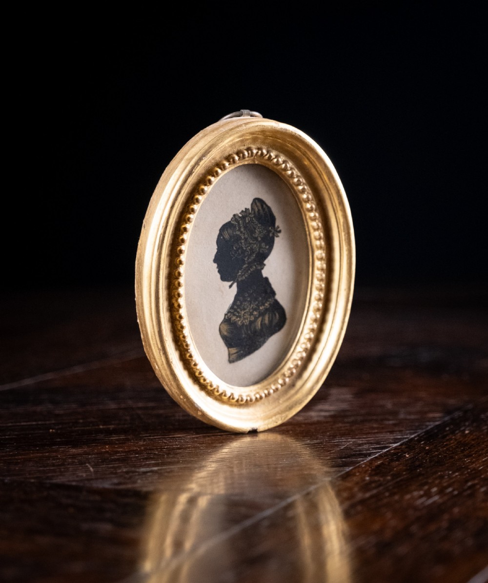 An oval early nineteenth-century silhouette portrait of a lady shown in profile with gold detailing, housed in a beaded gilded frame. View V