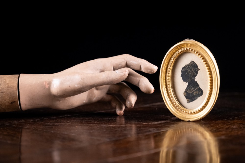 An oval early nineteenth-century silhouette portrait of a lady shown in profile with gold detailing, housed in a beaded gilded frame. View VII