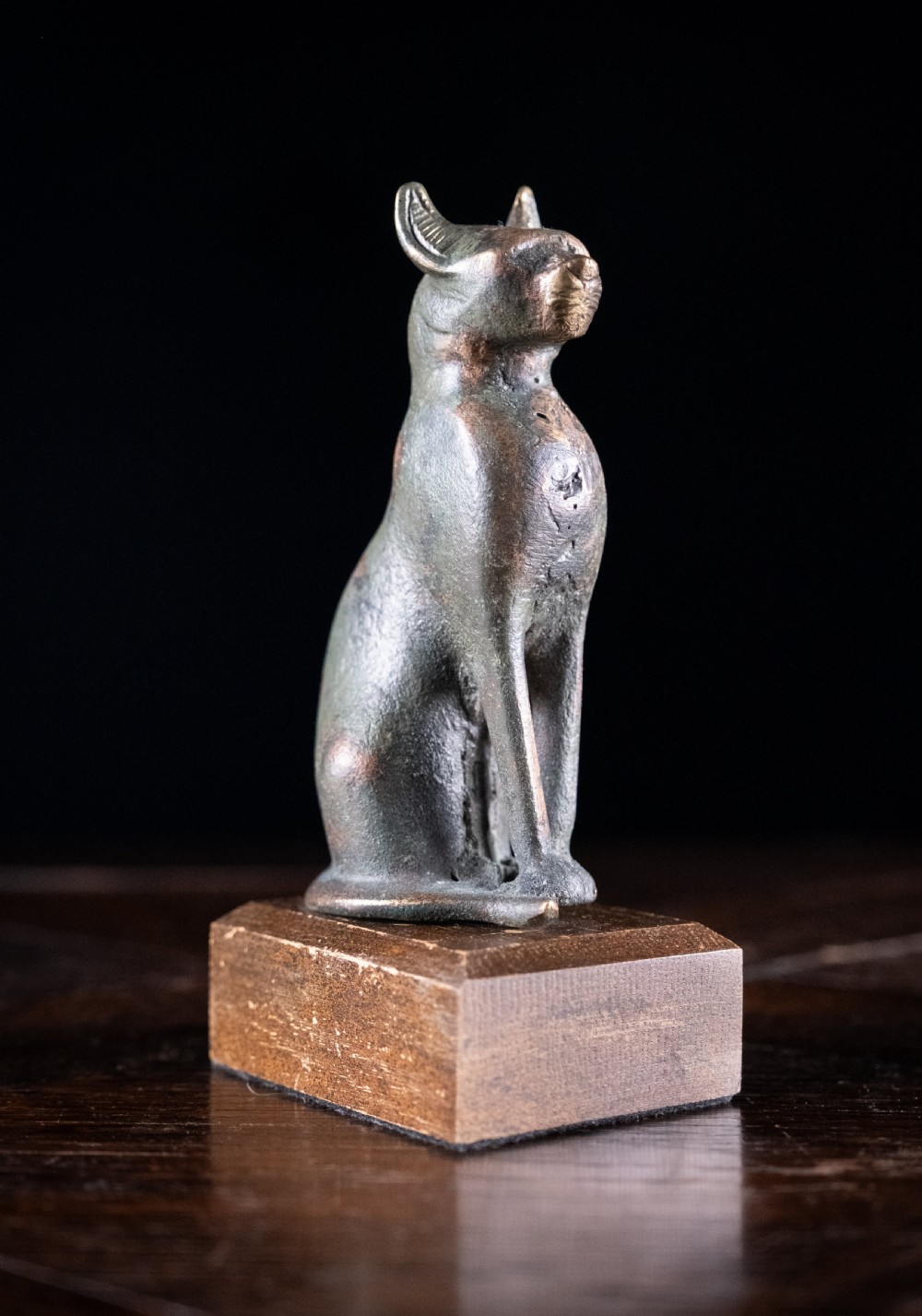 A dark patinated bronze figure of a seated Egyptian cat mounted on a wooden rectangular base.