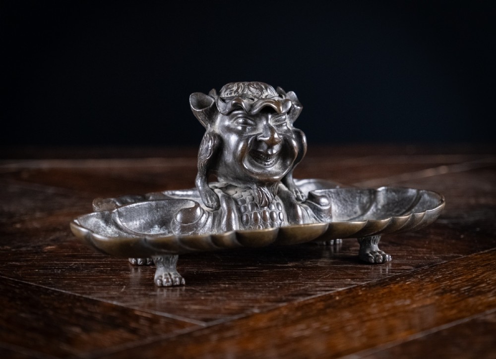 A 19th-century patinated bronze inkstand featuring a central sculpted grotesque face above a fluted pen tray raised on small paw feet.