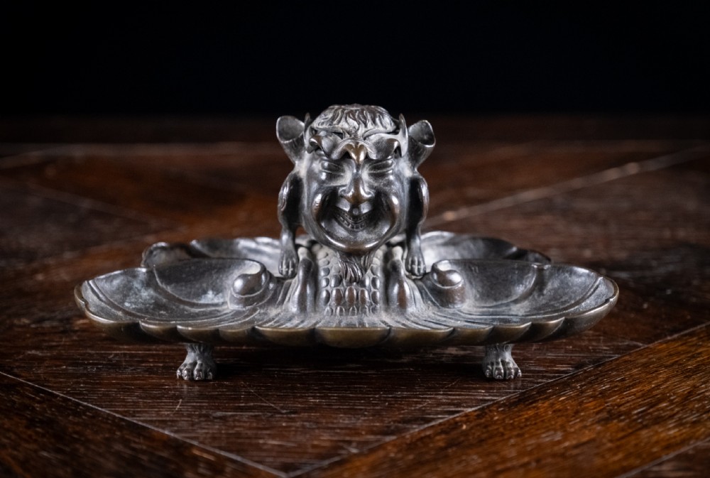 A 19th-century patinated bronze inkstand featuring a central sculpted grotesque face above a fluted pen tray raised on small paw feet. View VI
