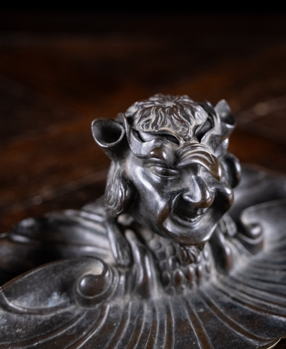 A 19th-century patinated bronze inkstand featuring a central sculpted grotesque face above a fluted pen tray raised on small paw feet. View VIII