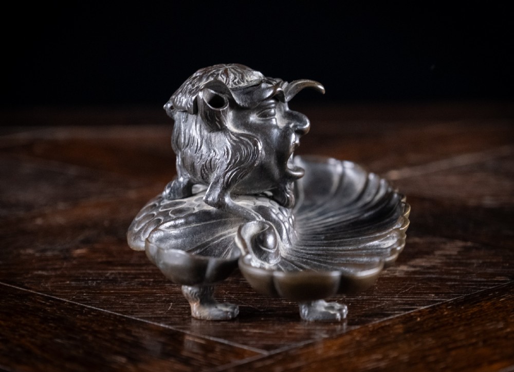A 19th-century patinated bronze inkstand featuring a central sculpted grotesque face above a fluted pen tray raised on small paw feet. View X