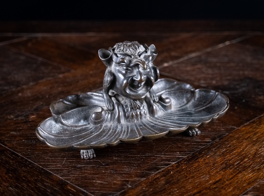 A 19th-century patinated bronze inkstand featuring a central sculpted grotesque face above a fluted pen tray raised on small paw feet. View XI