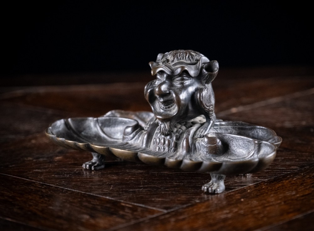 A 19th-century patinated bronze inkstand featuring a central sculpted grotesque face above a fluted pen tray raised on small paw feet. View XII