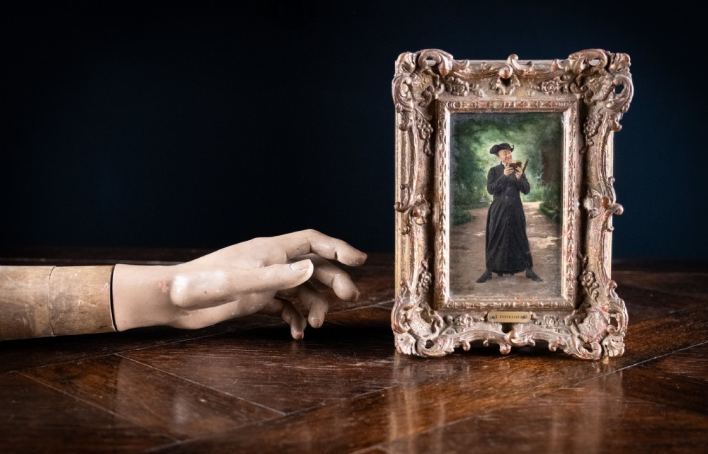 A 19th-century oil painting on panel depicting a smiling clergyman reading a book, set within a heavily carved rococo gilt frame. View VI