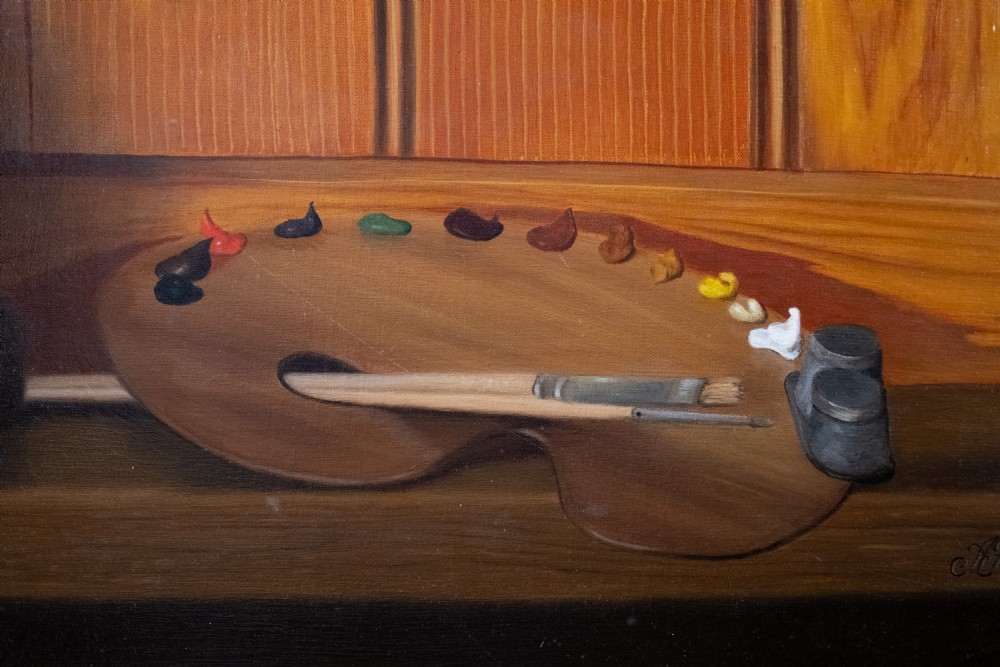 An oil painting depicting a human skull resting on a bound book alongside an artist palette, brushes, and a pinned sketch against a vertical timber panel background. View V