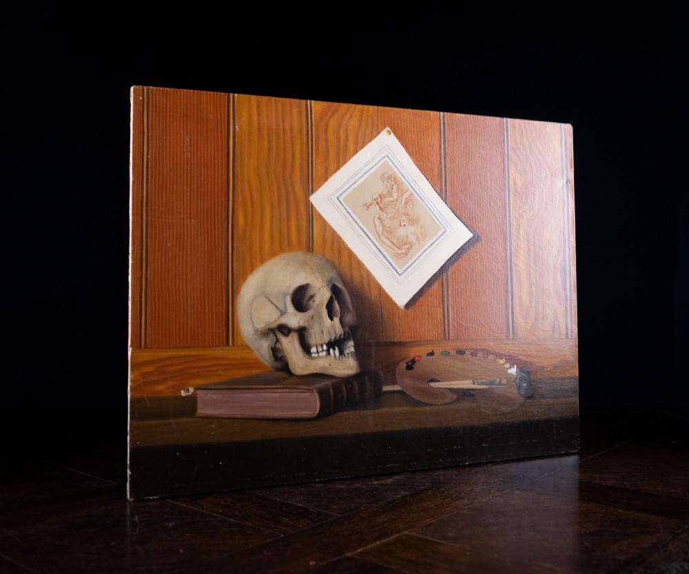 An oil painting depicting a human skull resting on a bound book alongside an artist palette, brushes, and a pinned sketch against a vertical timber panel background. View IX