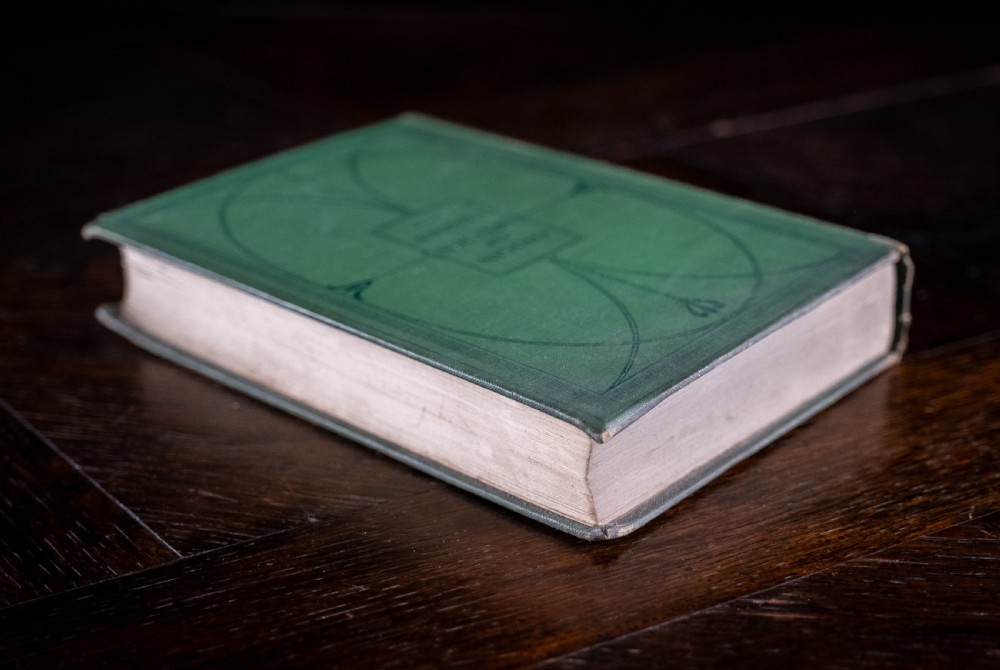 A green cloth-bound antique book standing vertically with gold embossed title lettering on the spine. View IV