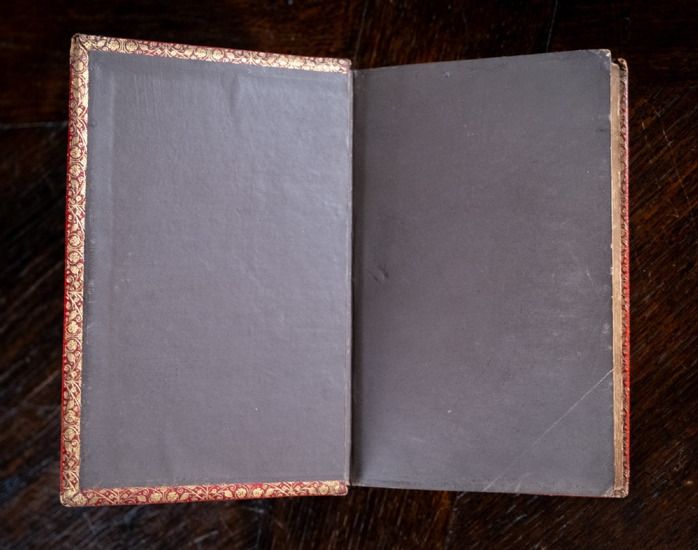 A Victorian red leather-bound book featuring detailed gold leaf tooling on the spine and covers standing upright. View VI