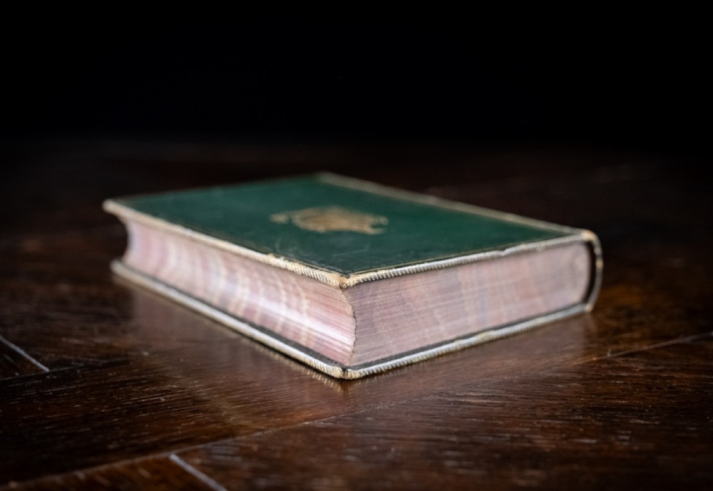 A Victorian leather-bound book standing upright, featuring green boards with a gilt crest and a brown leather spine decorated with gold tooling. View VI