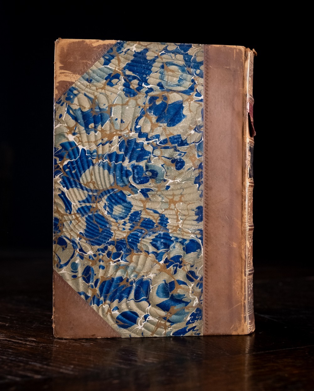An 1864 half leather bound book featuring a brown gold-tooled spine with raised bands and blue marbled paper boards. View V