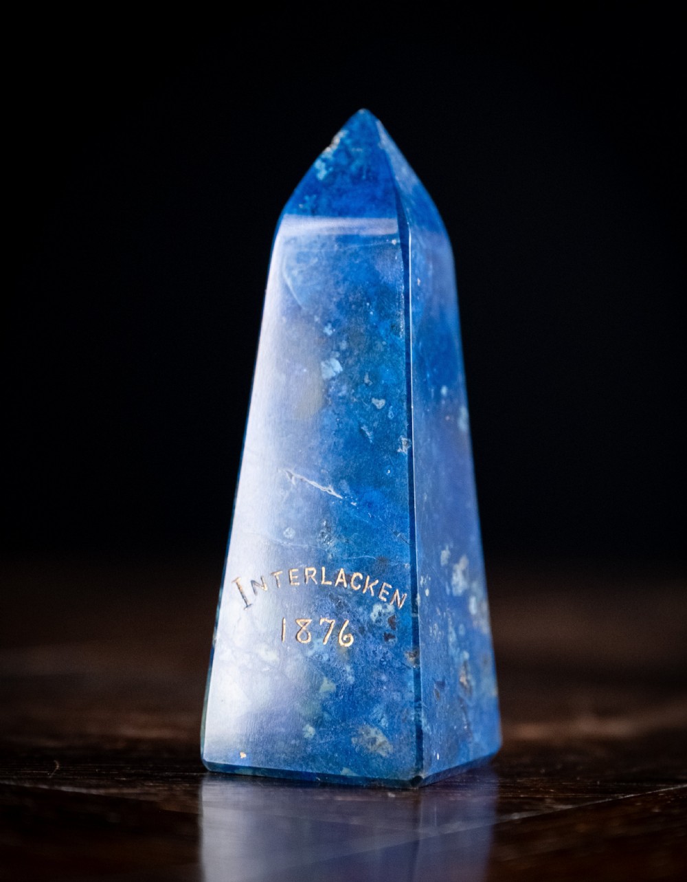 A polished deep blue lapis lazuli obelisk engraved with gilt text reading Interlacken 1876 near the base. View II