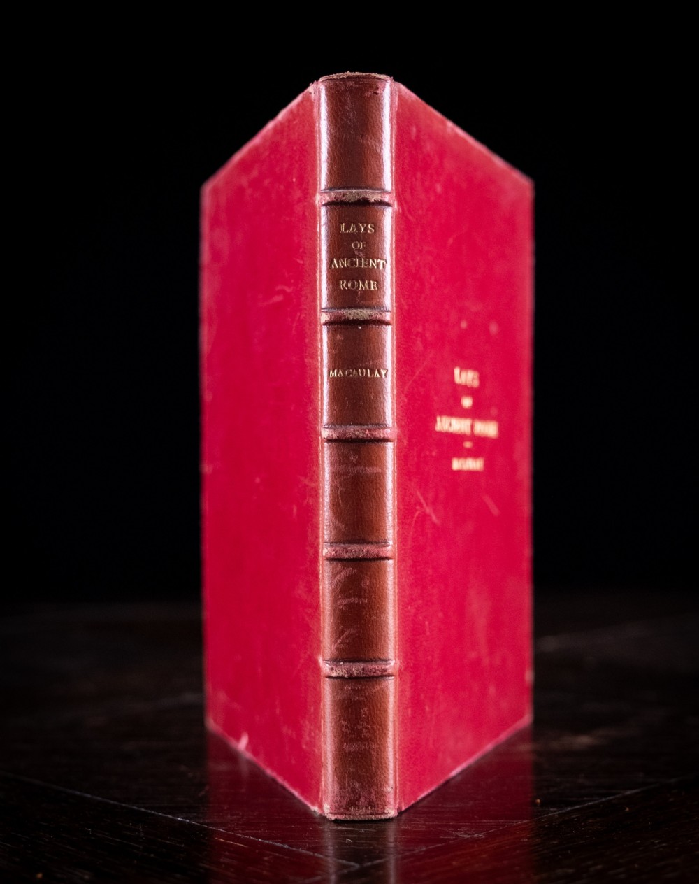 A red leather-bound edition of Lays of Ancient Rome by Macaulay, featuring raised spine bands and gilt lettering.