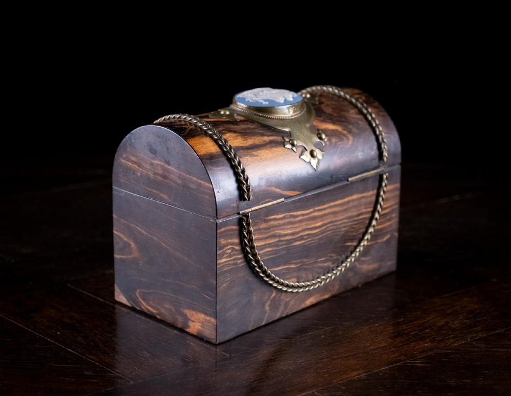 A Victorian domed coromandel wood casket featuring a central blue jasperware cameo medallion set within engraved brass mounts and a twisted brass border. View X