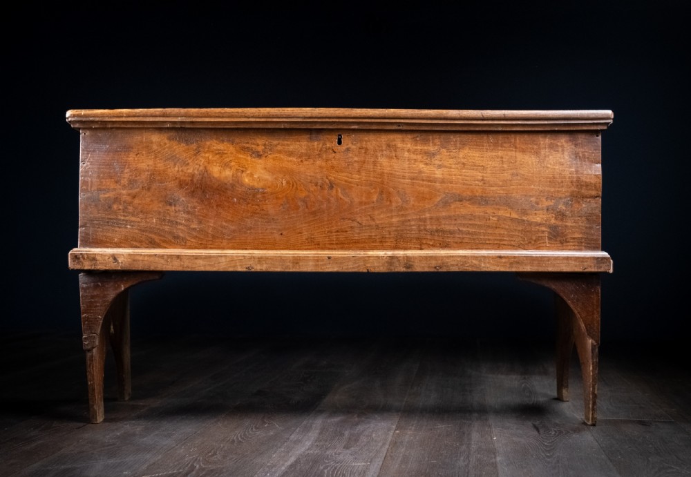 A seventeenth-century elm six-plank coffer featuring a hinged lid, raised bootjack side ends, and visible grain patterns against a dark background. View II