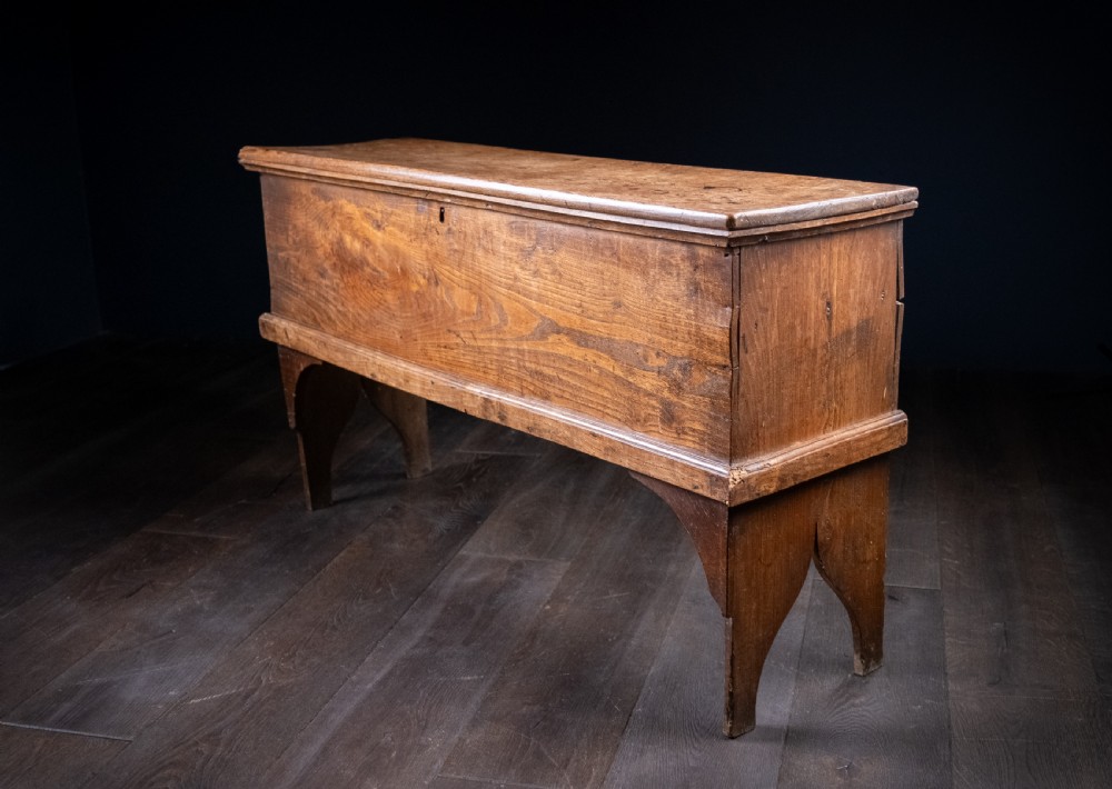 A seventeenth-century elm six-plank coffer featuring a hinged lid, raised bootjack side ends, and visible grain patterns against a dark background. View III