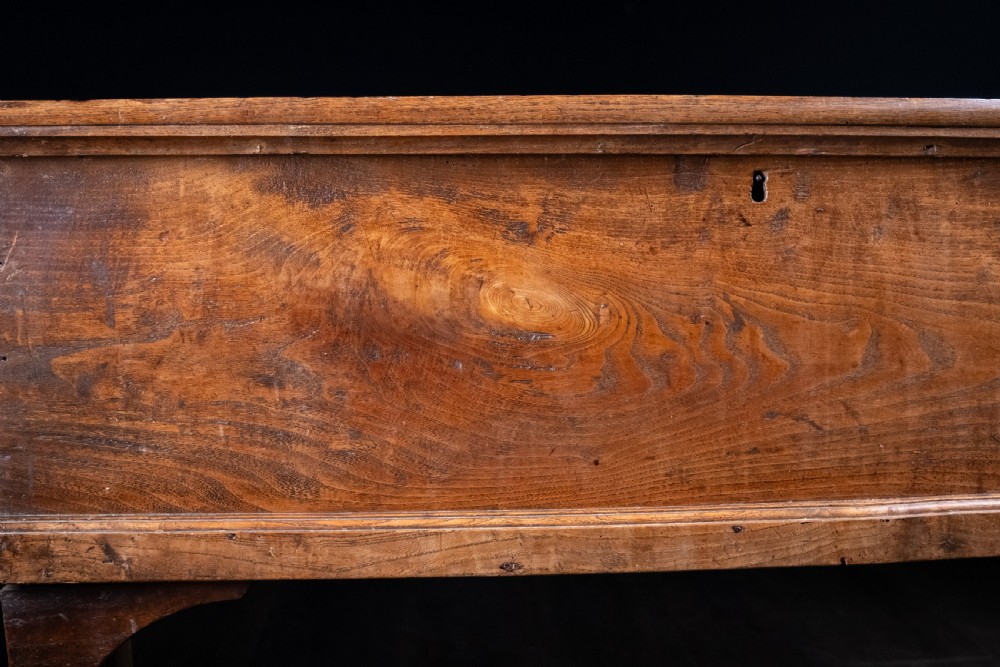 A seventeenth-century elm six-plank coffer featuring a hinged lid, raised bootjack side ends, and visible grain patterns against a dark background. View IV