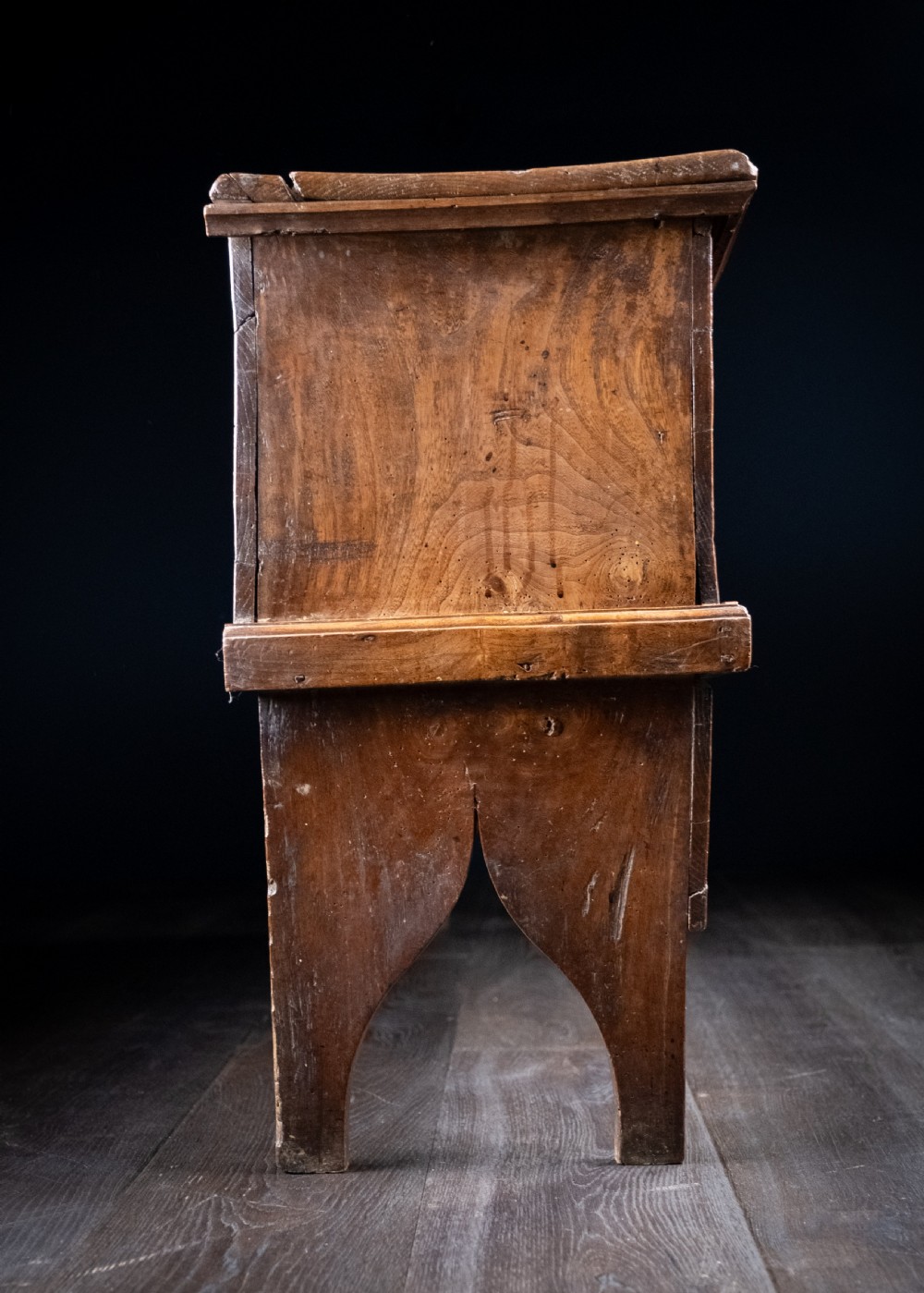 A seventeenth-century elm six-plank coffer featuring a hinged lid, raised bootjack side ends, and visible grain patterns against a dark background. View VII