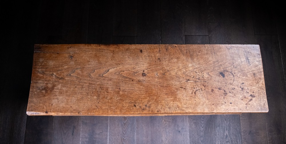 A seventeenth-century elm six-plank coffer featuring a hinged lid, raised bootjack side ends, and visible grain patterns against a dark background. View IX