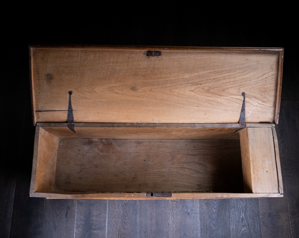 A seventeenth-century elm six-plank coffer featuring a hinged lid, raised bootjack side ends, and visible grain patterns against a dark background. View X