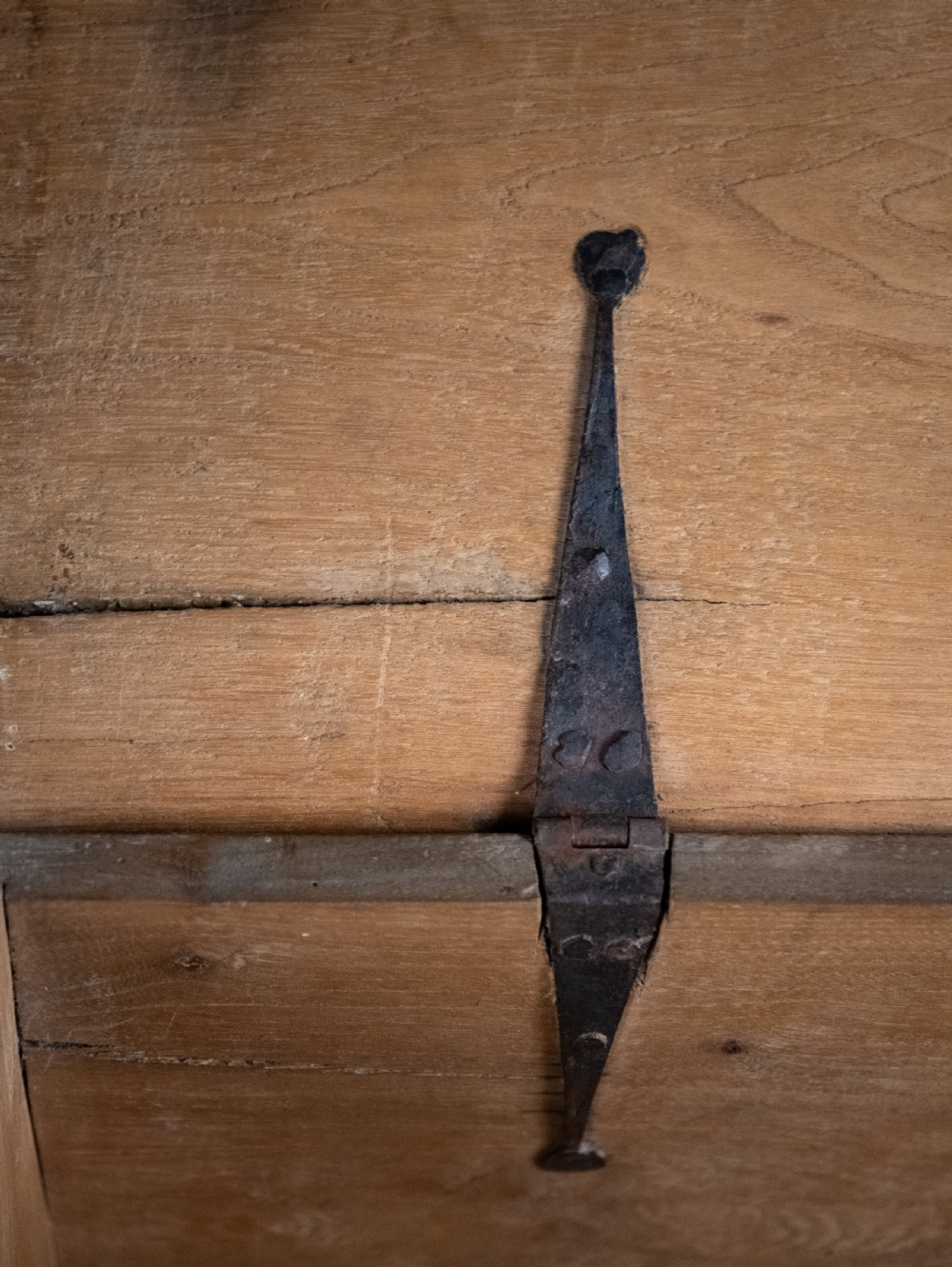 A seventeenth-century elm six-plank coffer featuring a hinged lid, raised bootjack side ends, and visible grain patterns against a dark background. View XI
