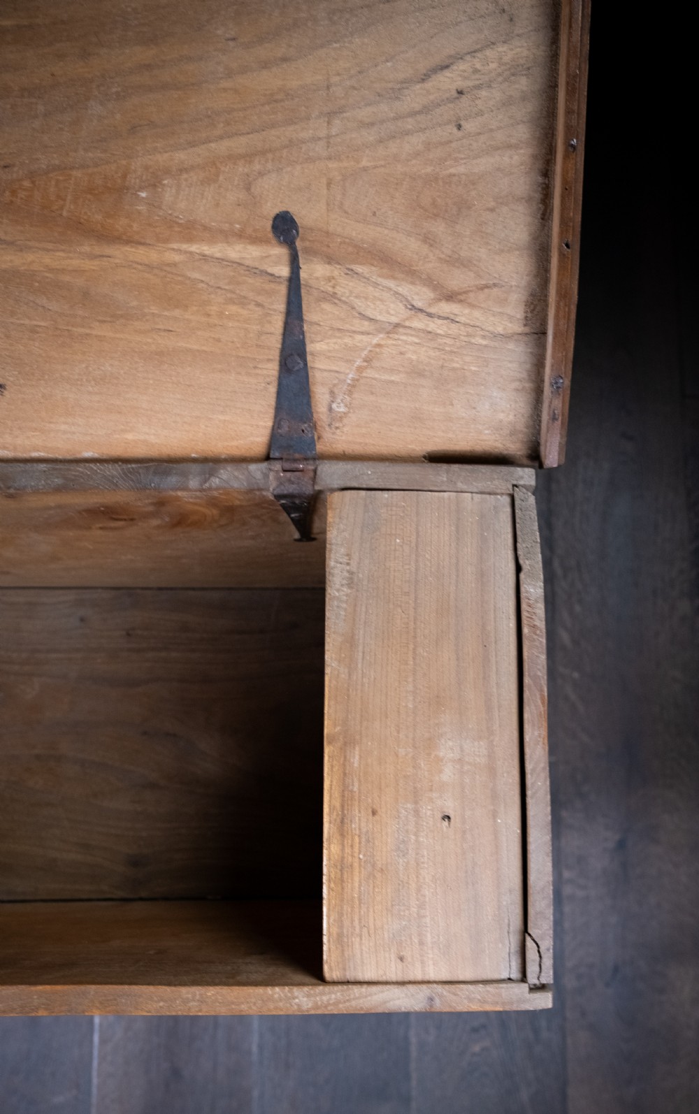 A seventeenth-century elm six-plank coffer featuring a hinged lid, raised bootjack side ends, and visible grain patterns against a dark background. View XII