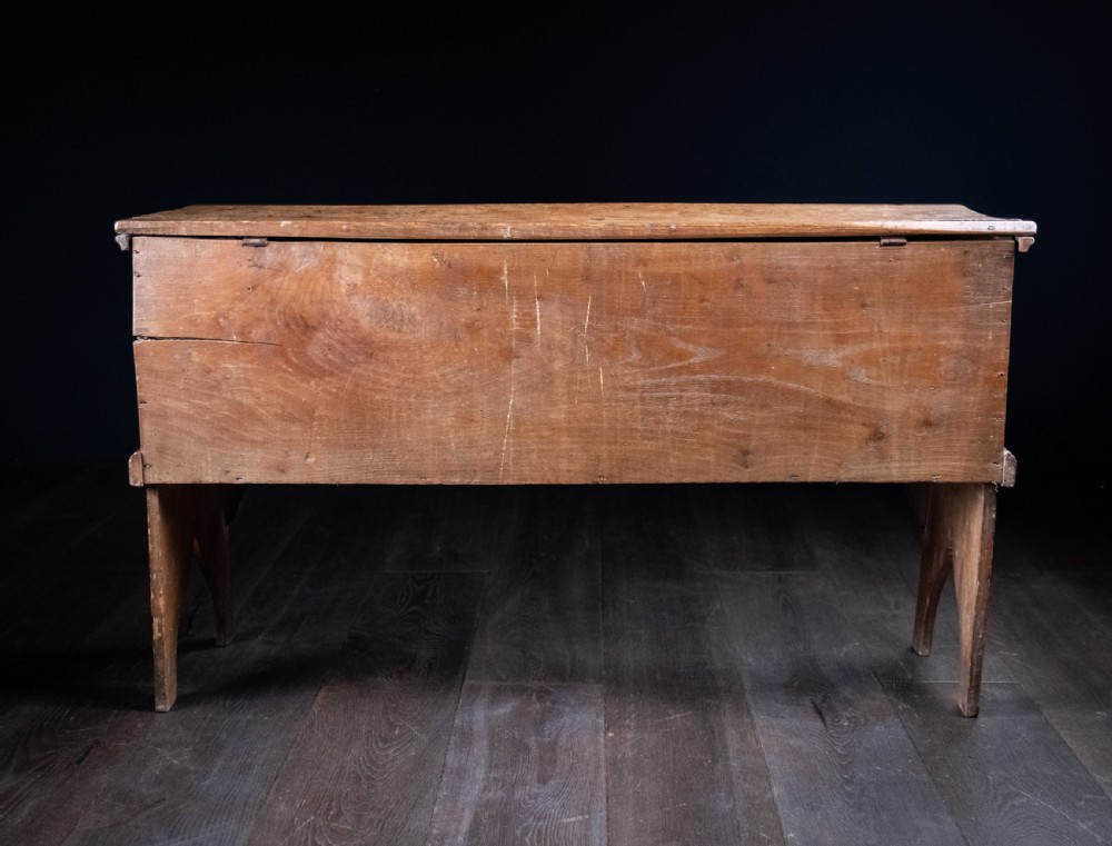 A seventeenth-century elm six-plank coffer featuring a hinged lid, raised bootjack side ends, and visible grain patterns against a dark background. View XIV