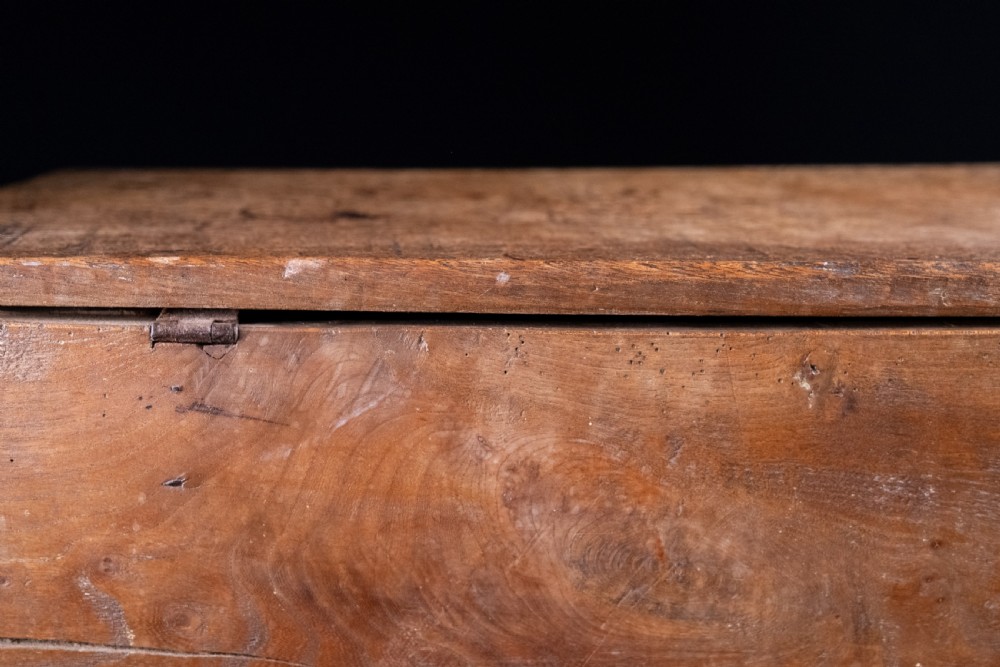 A seventeenth-century elm six-plank coffer featuring a hinged lid, raised bootjack side ends, and visible grain patterns against a dark background. View XV