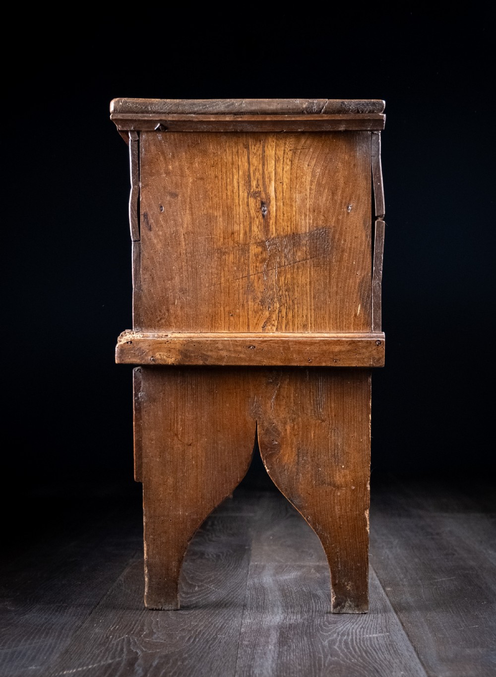 A seventeenth-century elm six-plank coffer featuring a hinged lid, raised bootjack side ends, and visible grain patterns against a dark background. View XVII