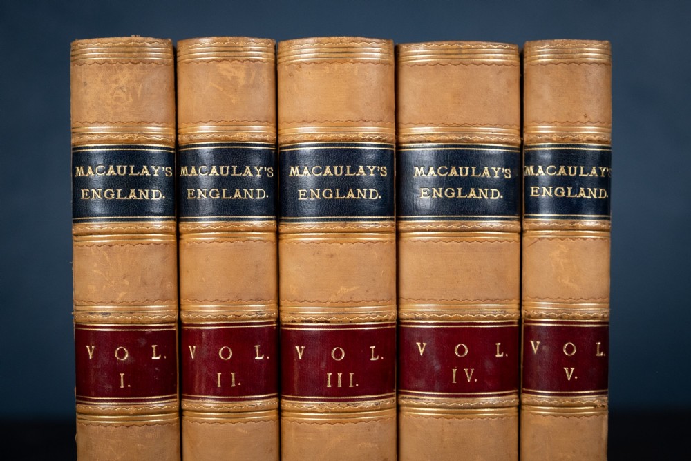 A five-volume set of Victorian leather-bound books with tan calfskin spines, gilt tooling, and contrasting red and navy spine labels standing vertically. View II