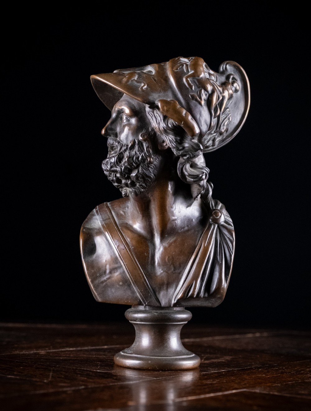 A patinated dark brown French bronze bust depicting the classical figure of Ajax wearing a detailed helmet, set upon a turned circular pedestal.