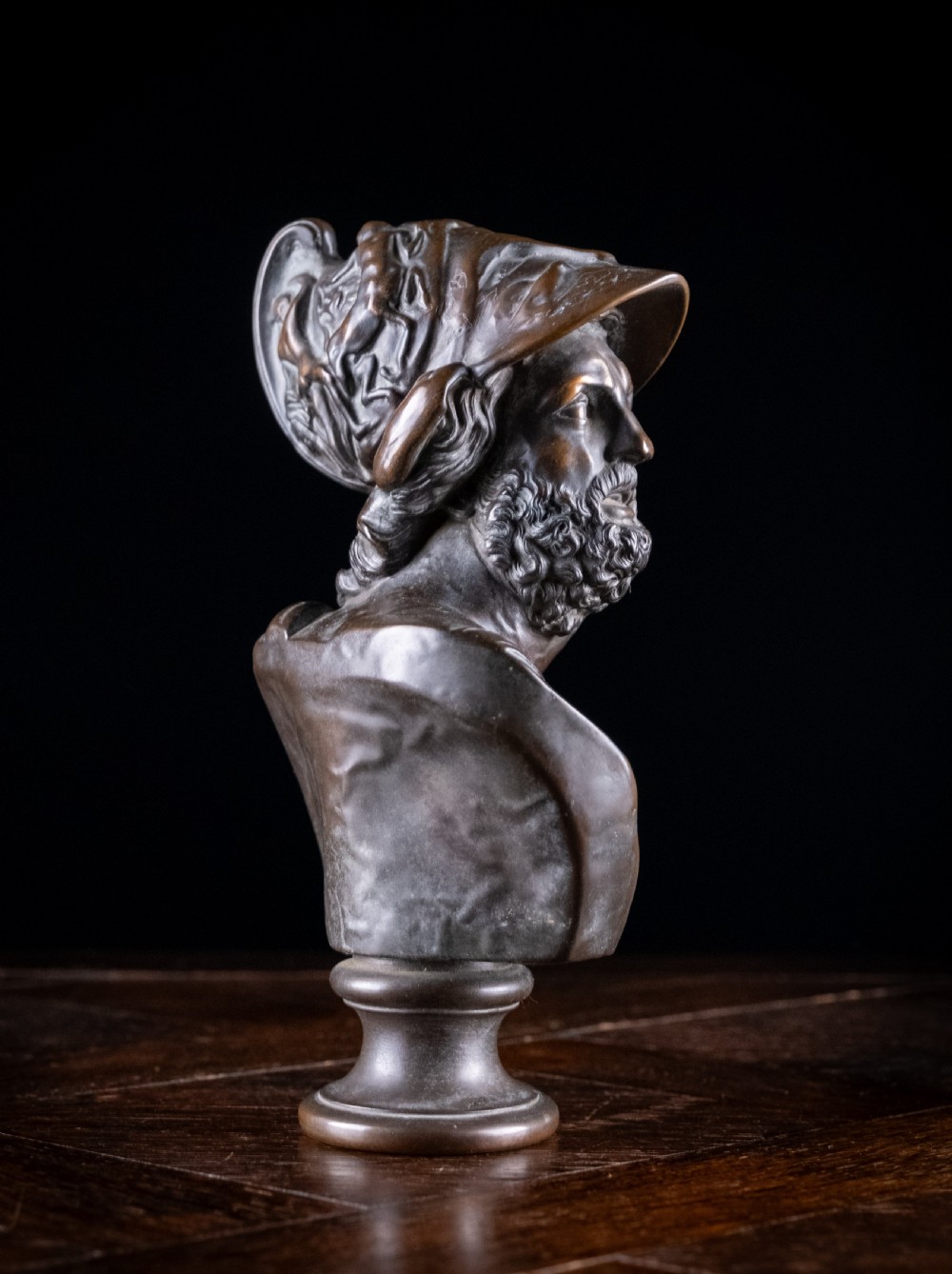 A patinated dark brown French bronze bust depicting the classical figure of Ajax wearing a detailed helmet, set upon a turned circular pedestal. View III