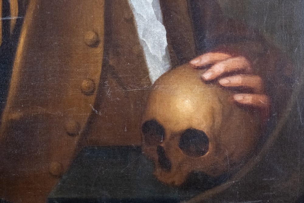 An 18th-century oil painting depicting a gentleman with a white powdered wig wearing a brown coat and resting his hand upon a human skull. View III