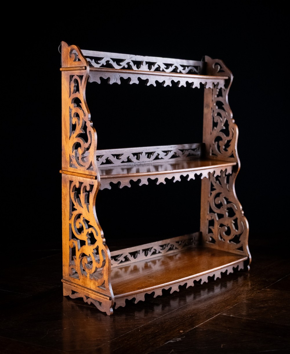 A three-tier Victorian mahogany wall shelf featuring open fretwork sides, pierced scroll decoration, and serrated apron trim.