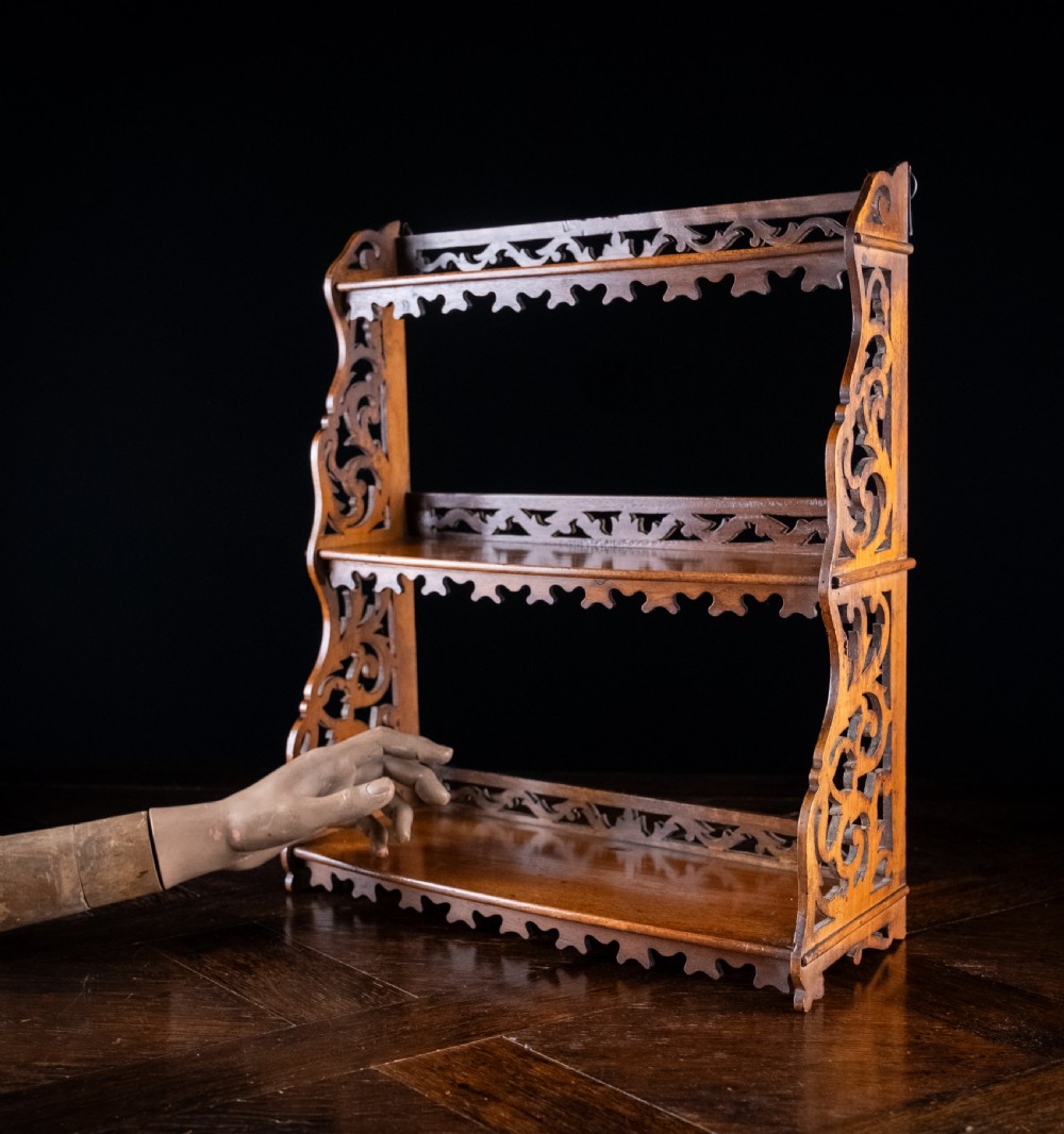 A three-tier Victorian mahogany wall shelf featuring open fretwork sides, pierced scroll decoration, and serrated apron trim. View II