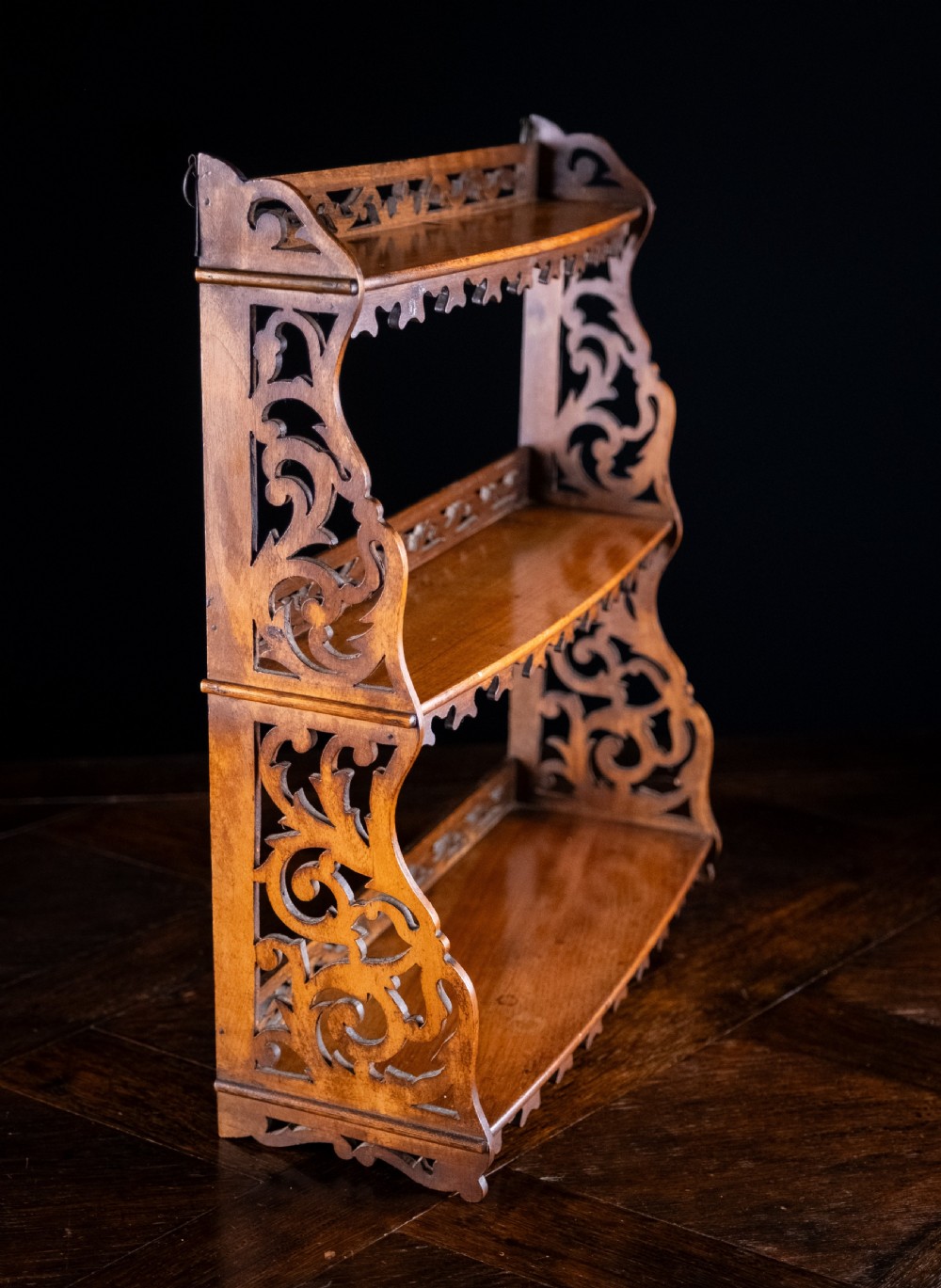 A three-tier Victorian mahogany wall shelf featuring open fretwork sides, pierced scroll decoration, and serrated apron trim. View III