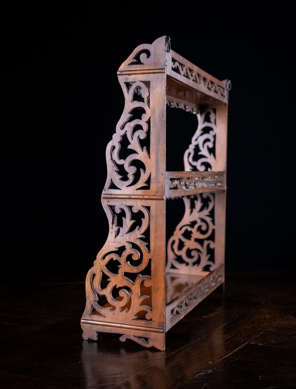 A three-tier Victorian mahogany wall shelf featuring open fretwork sides, pierced scroll decoration, and serrated apron trim. View VIII