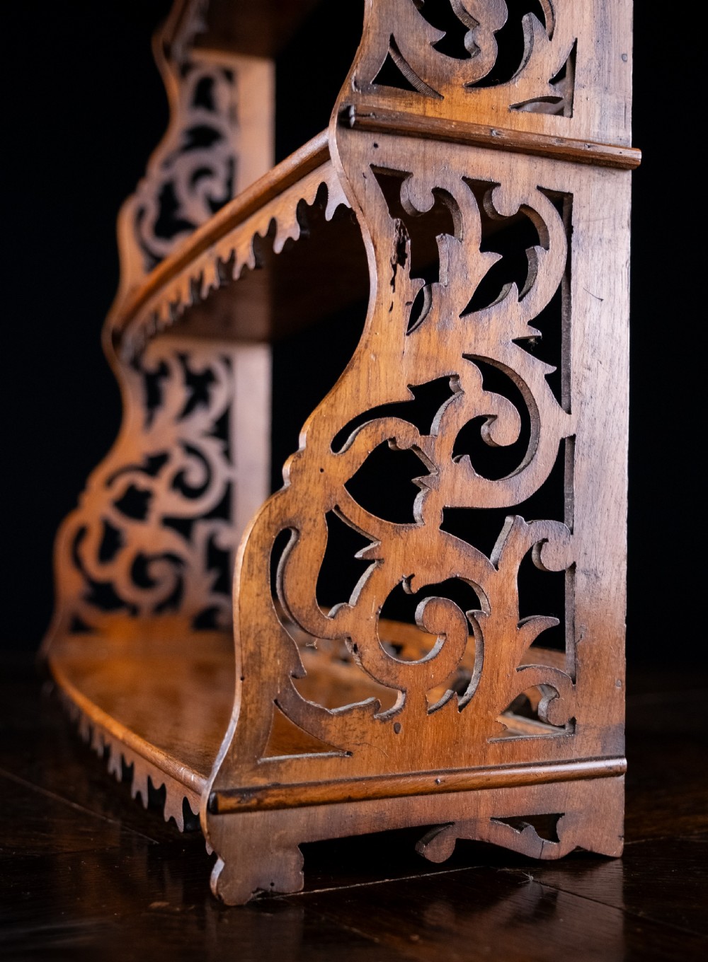 A three-tier Victorian mahogany wall shelf featuring open fretwork sides, pierced scroll decoration, and serrated apron trim. View IX