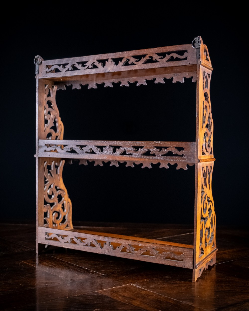 A three-tier Victorian mahogany wall shelf featuring open fretwork sides, pierced scroll decoration, and serrated apron trim. View X