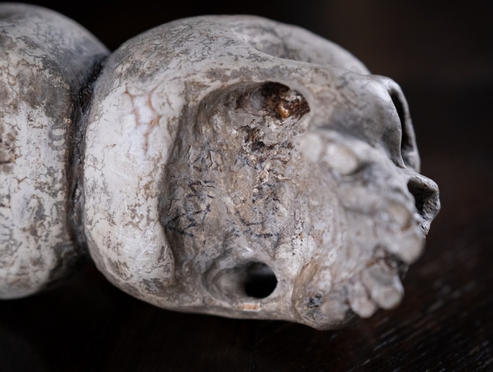 A pair of small carved off-white skull sculptures suspended from a twisted metal chain attached to a black wrought iron stand. View XV