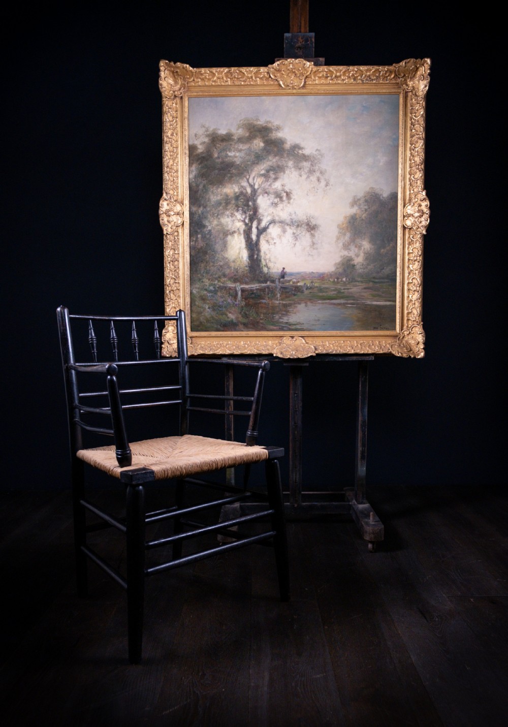 An impressionist oil painting depicting a rural countryside landscape with a large tree by a river, enclosed within an ornate gilded frame. View III