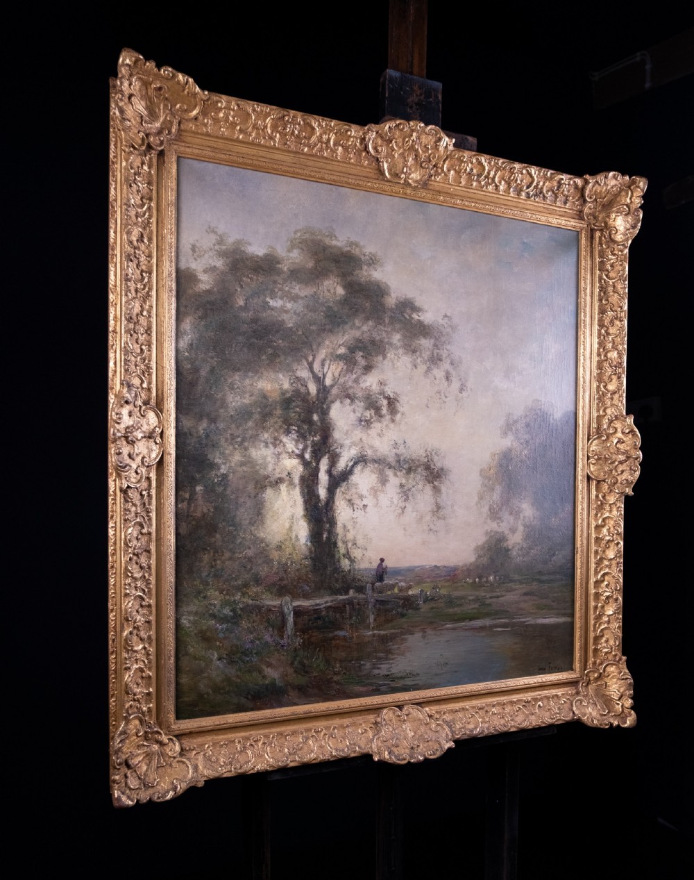 An impressionist oil painting depicting a rural countryside landscape with a large tree by a river, enclosed within an ornate gilded frame. View XI
